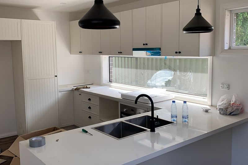 White kitchen with black pendant lights and a black mixer tap