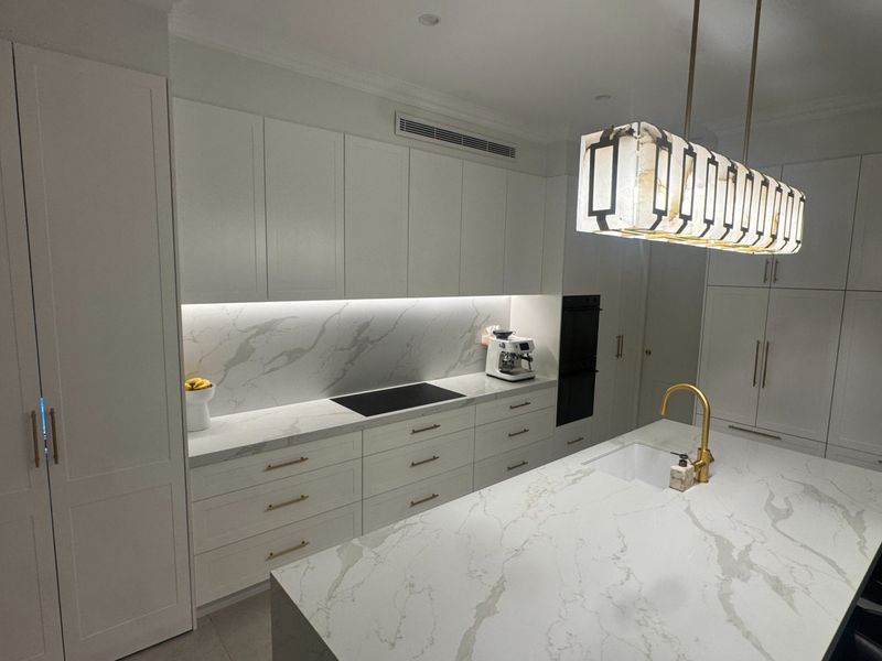 A close view of a marble benchtop and induction cooktop, finished with a gold tap and floor-to-ceiling cabinetry.