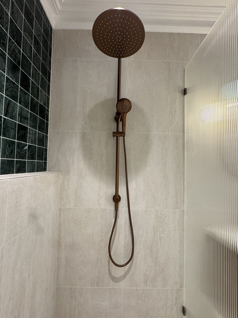 A bronze rainfall shower and fluted glass screen finish this green mosaic-tiled bathroom.