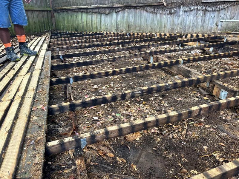 Old deck boards lifted to expose the original bearers and joists, sitting close to the soil