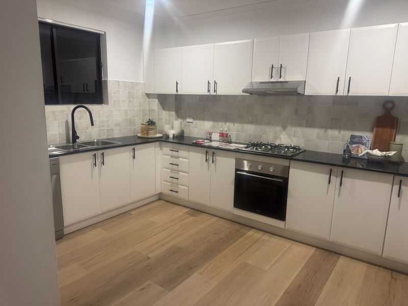 L-shaped kitchen finished with white cabinetry, a gas cooktop and timber floorboards.