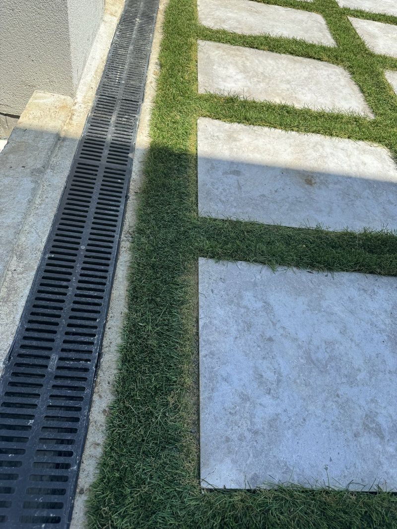 Channel drain set between pavers and turf to carry surface water away