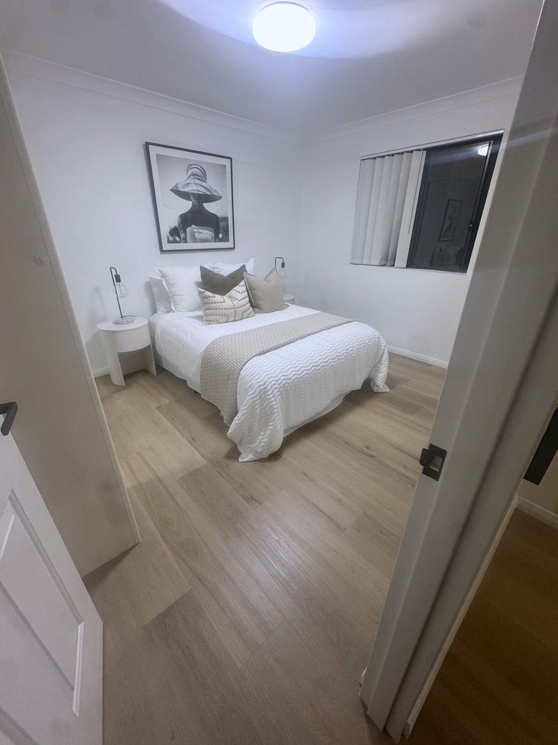 Bedroom finished with a made bed, bedside lamps and framed art above the headboard, timber floorboards throughout