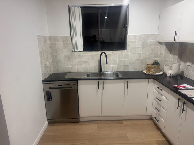 A stainless steel dishwasher and sink beneath a tiled splashback in this finished Sydney kitchen.