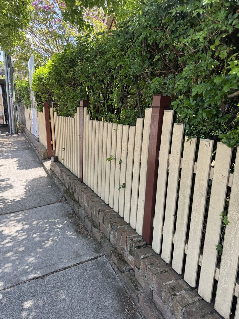 Restored picket fence with cream pickets and brown posts after the repair