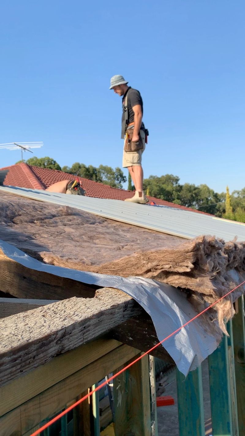Tradesperson fitting new roof sheeting over fresh insulation during a re-decking job