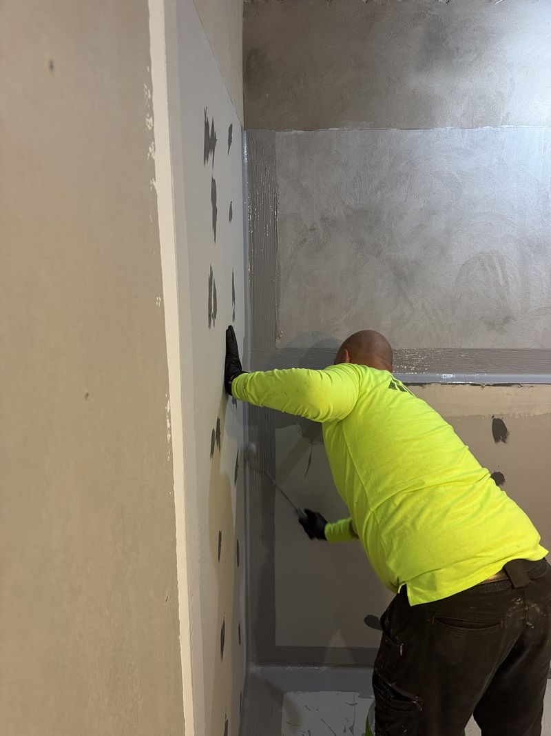 Tradesperson in hi-vis skimming a patched wall before painting