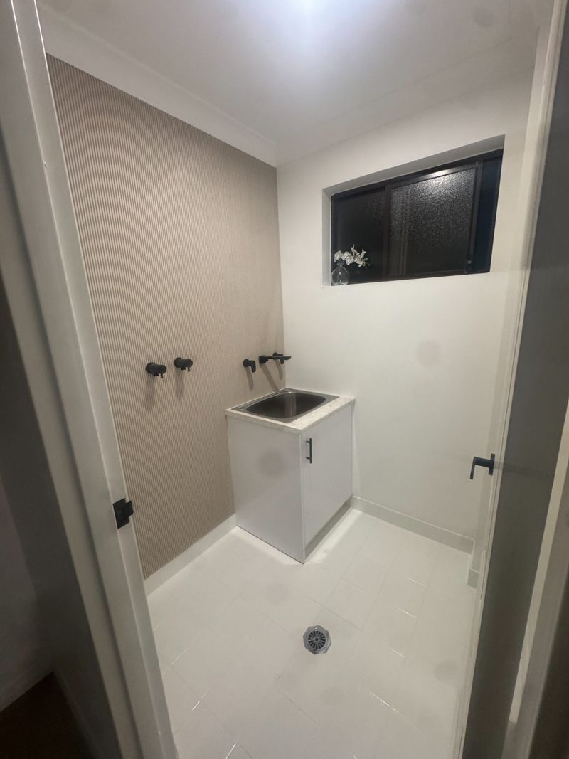 Finished laundry with a trough sink, wall taps and feature wallpaper.