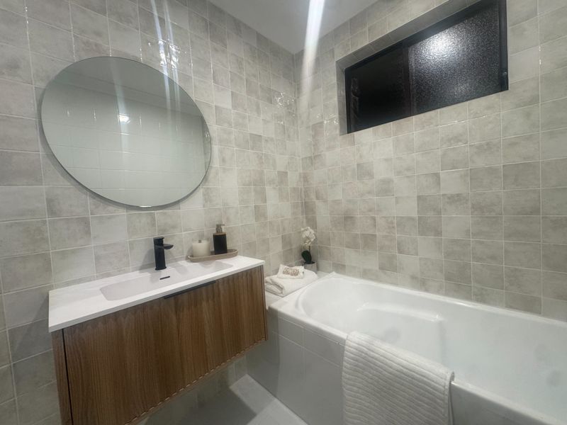 Round mirror and timber vanity beside a freestanding bath in this finished Sydney bathroom.
