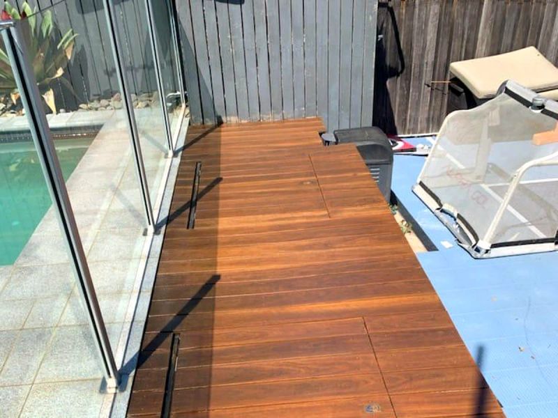 Oiled hardwood deck running alongside a glass pool fence