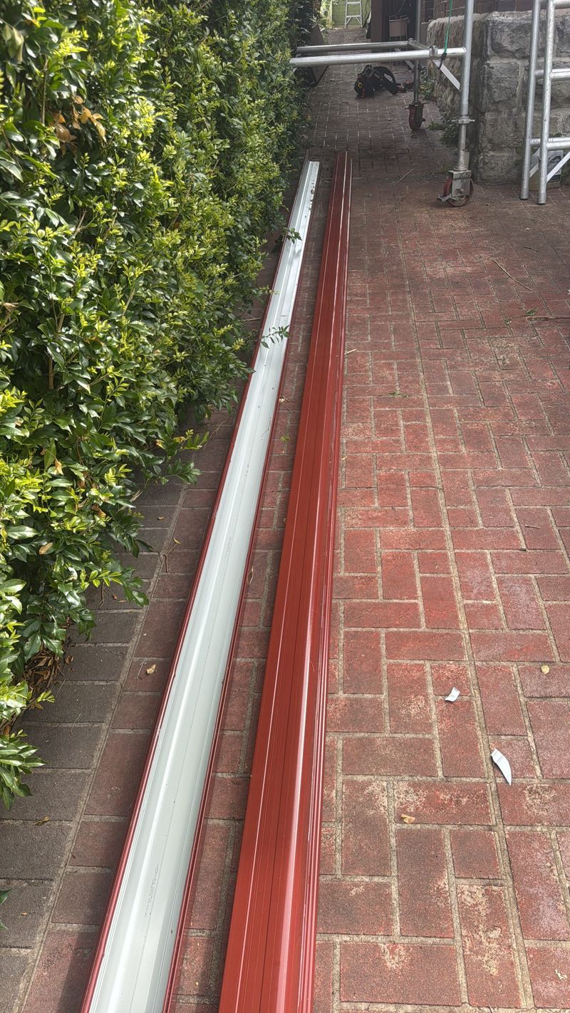 New red and white gutter and fascia lengths staged against a brick wall before installation