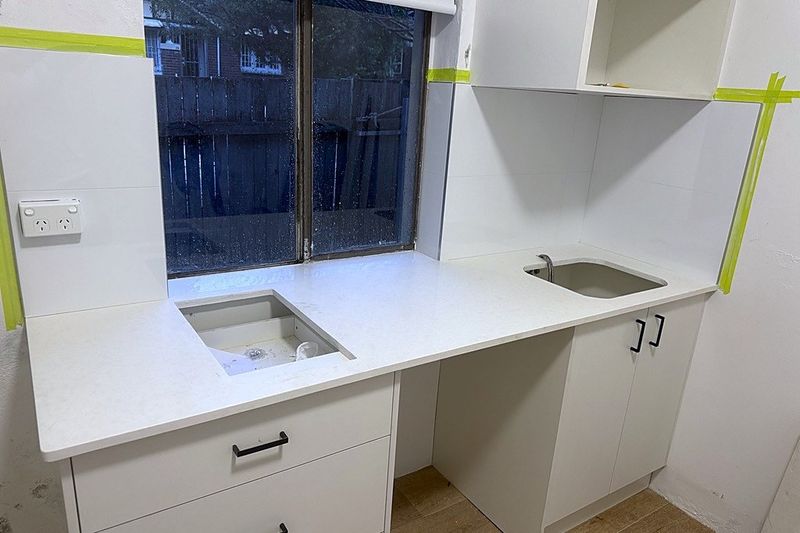 Stone benchtop and cabinetry installed before the splashback is tiled