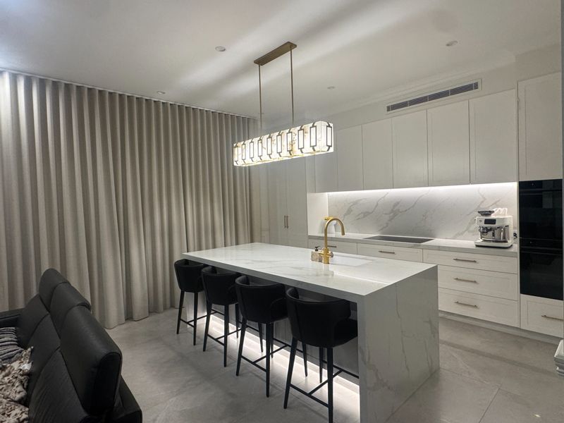 A marble kitchen island with black barstools opens onto a curtained living area in this Sydney home.